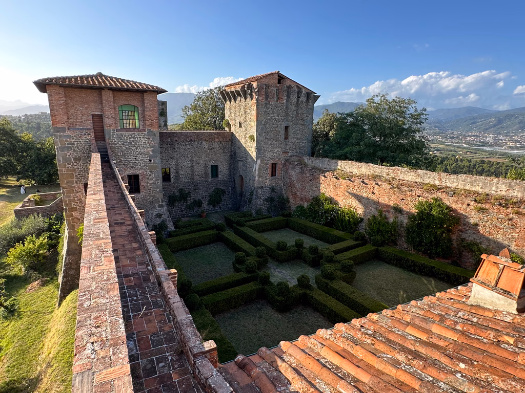The stone towers, walls and clipped garden of the Fortress of Montecarlo with hills beyond
