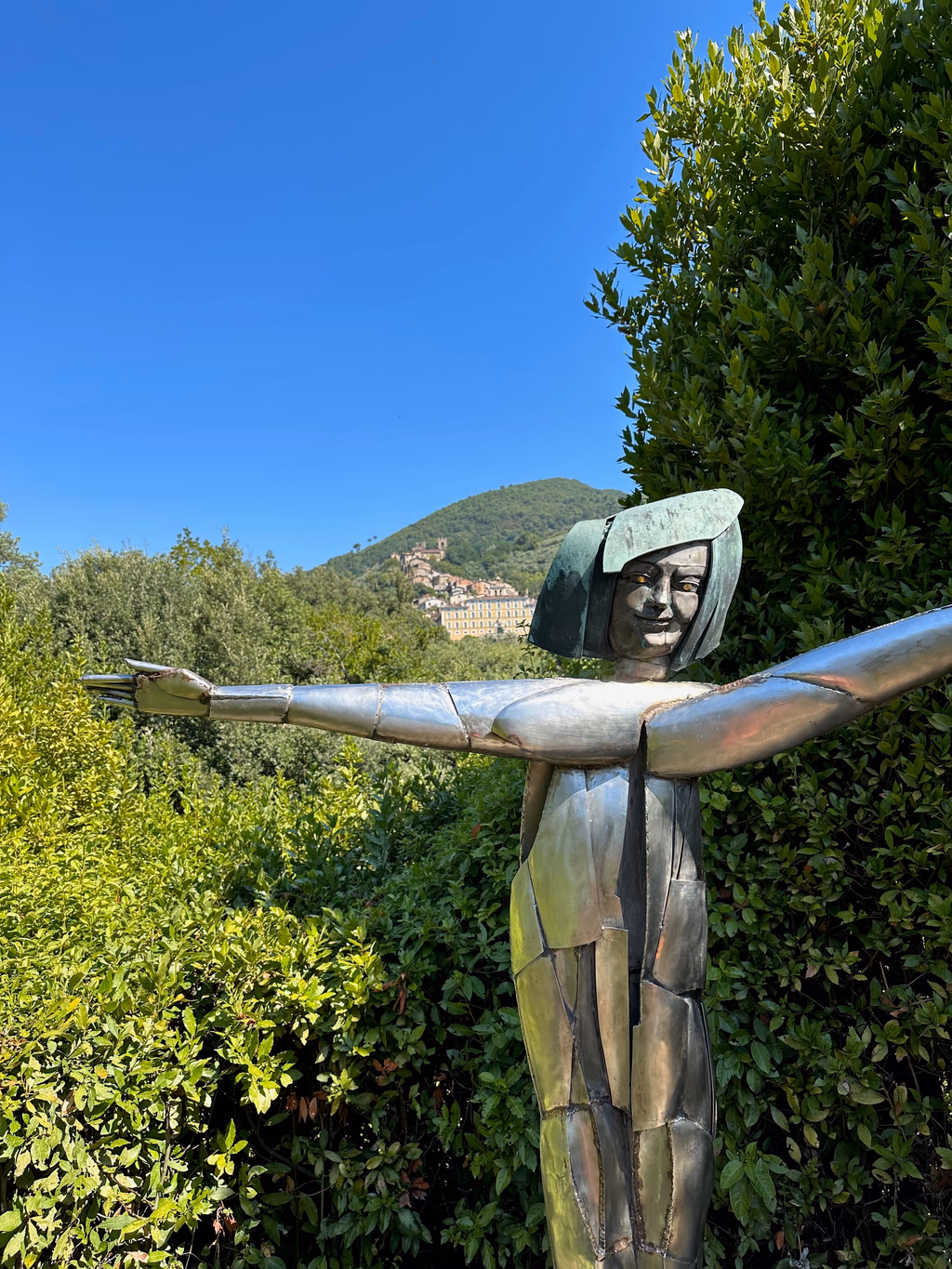 The metallic Fairy sculpture with old Collodi rising on the hillside behind her