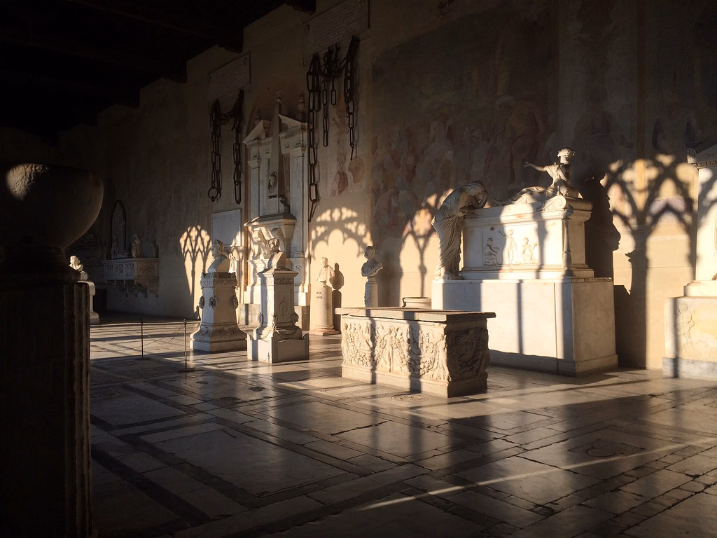 Sunlight falling across marble tombs and frescoes inside the Camposanto in Pisa
