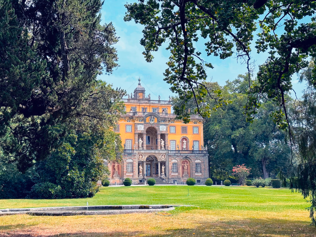 The orange front of Villa Torrigiani framed by trees at the end of its lawn